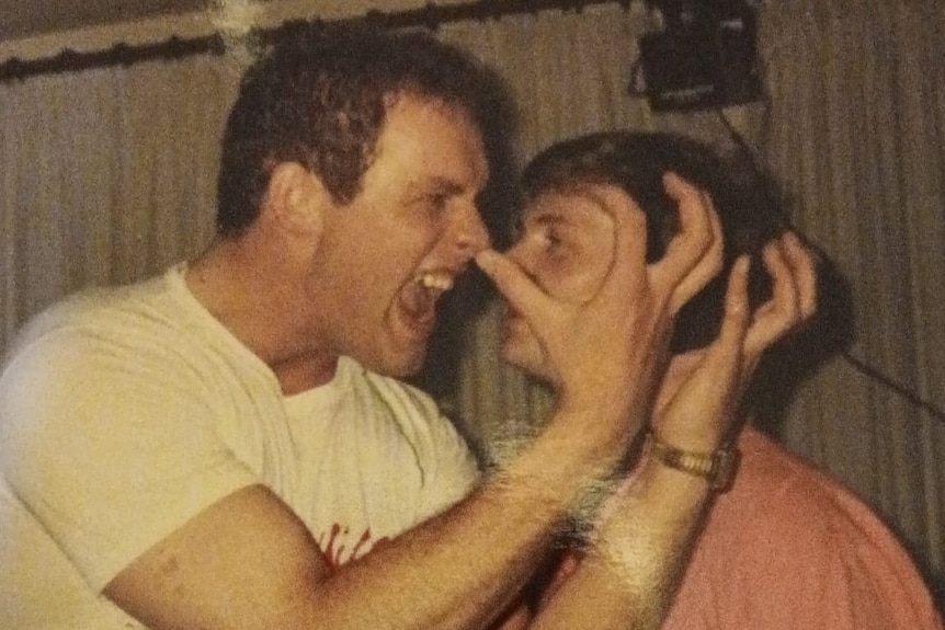 A man in a white shirt puling an angry face with his hands in the air standing close to a man in a red shirt.