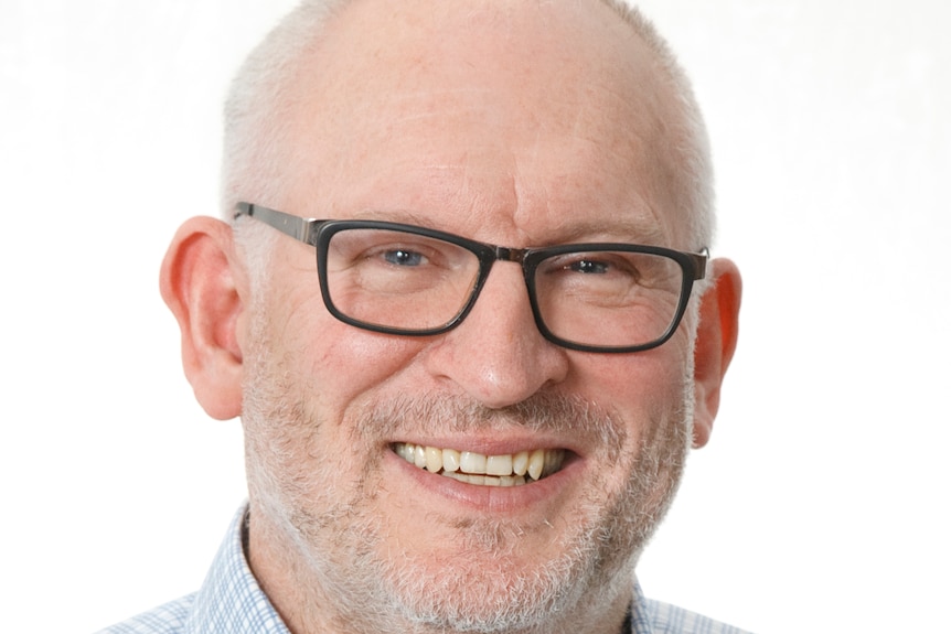 Man in a blue checkered shirt smiling with glasses.