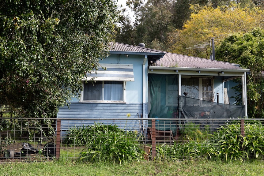 A blue weatherboard house, with white shutters and a fence.