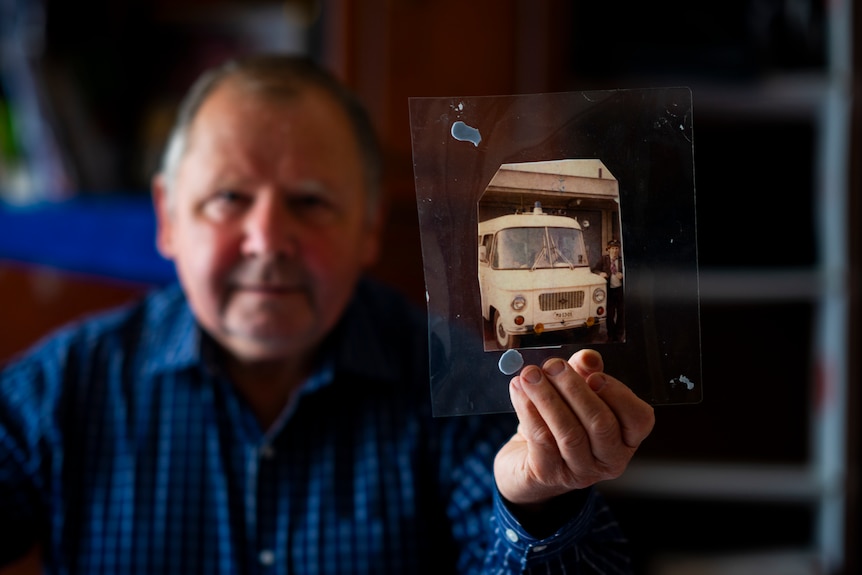 A man holds an old photograph of an ambulance towards the camera