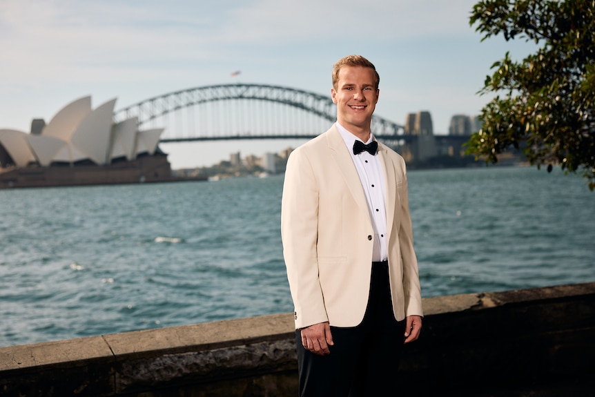 A blonde man in a suit overlooking Sydney Harbour and the Harbour Bridge