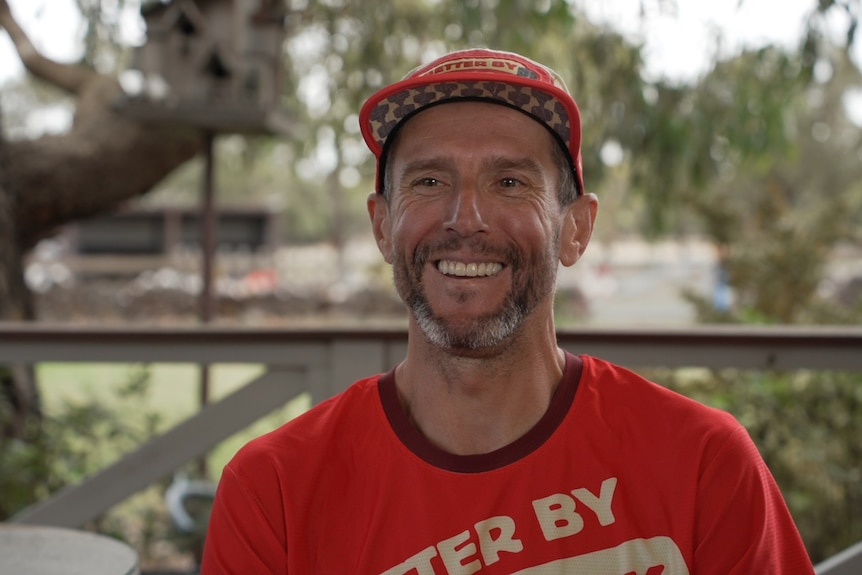 Tim Kacprzak wears a red hat and red s-hirt. He smiles at the camera.