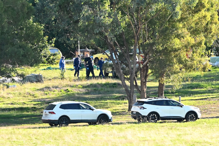 A pair of SUVs parked near some trees and a group of police on a country property.