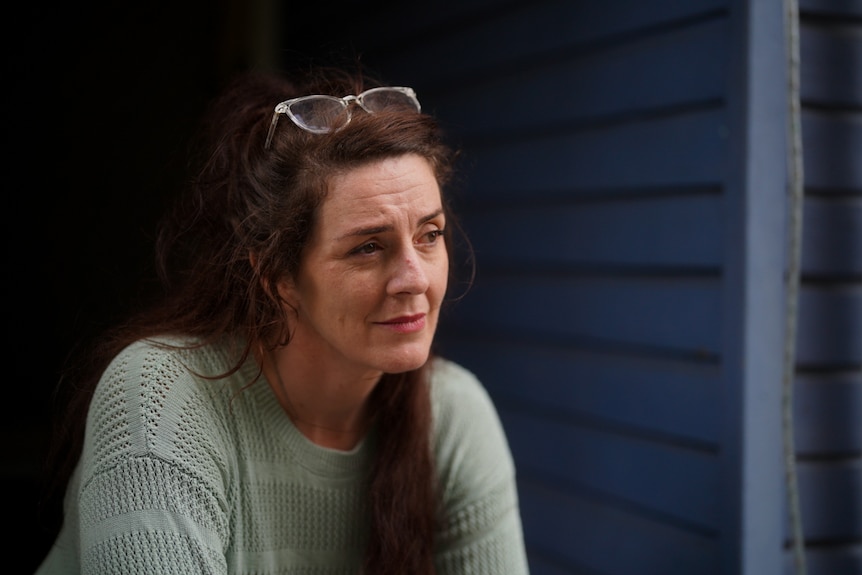 A woman stands in front of her home staring out pensively.