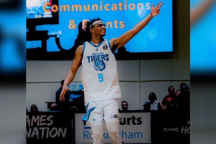 Roosevelt Williams Jr stands on a basketball court giving a salute to a crowd.