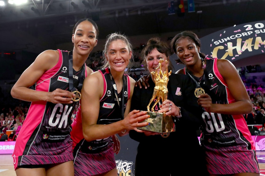 Defensive coach Cathy Fellows poses with the Super Netball trophy and her defenders