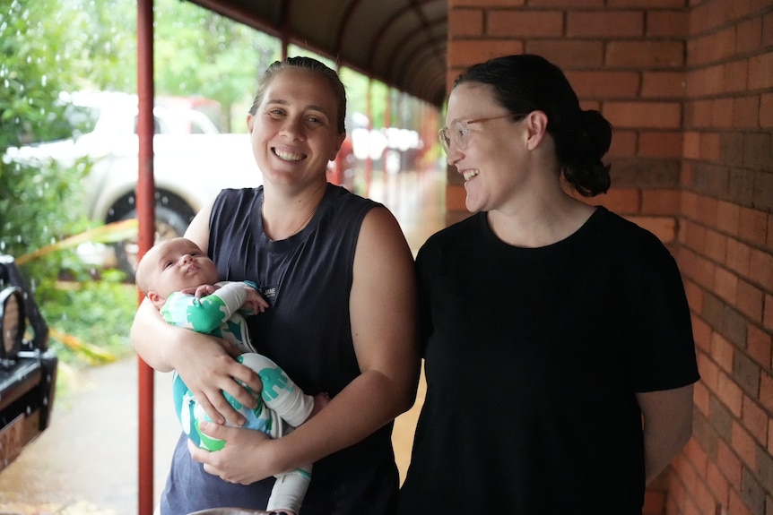 Two women smiling with one holding baby and the other looking at baby