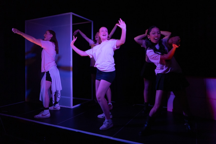 Young women with their arms in the air on a darkened stage. 