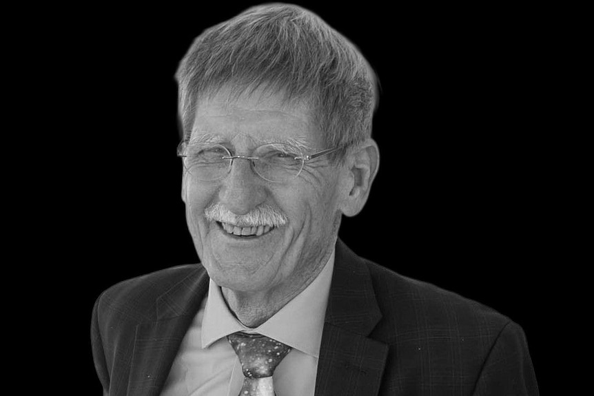 A man with a white moustache and spectacles, laughing.