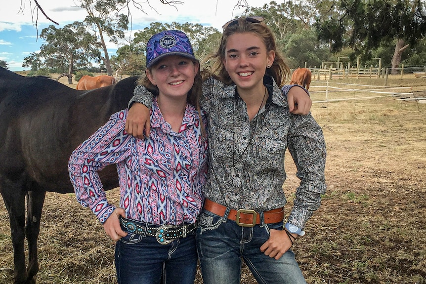 Two girls stand arm in arm in front of a horse