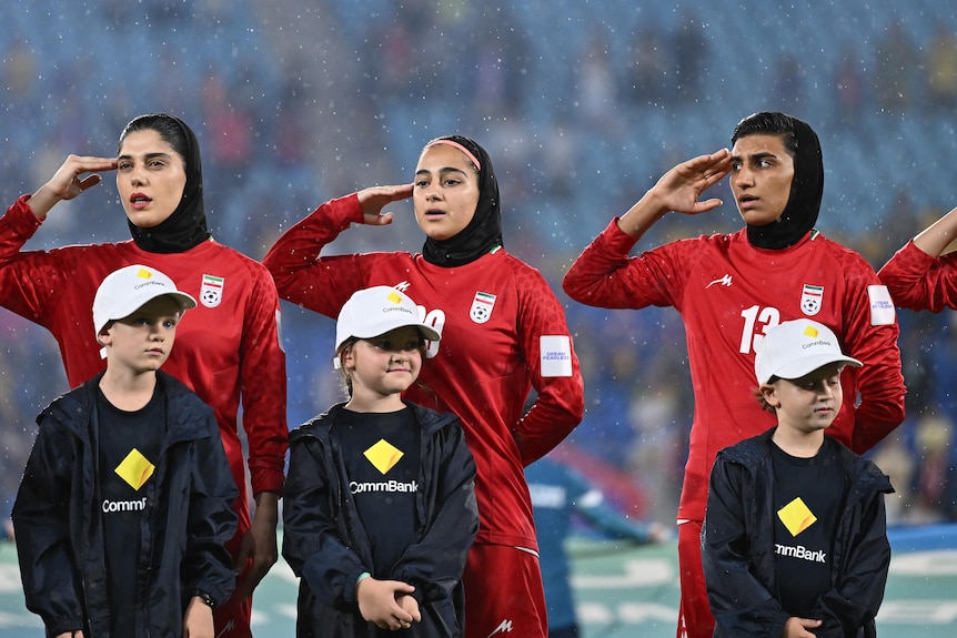 Players from the Iran women's football team salute and sing the national anthem before a game
