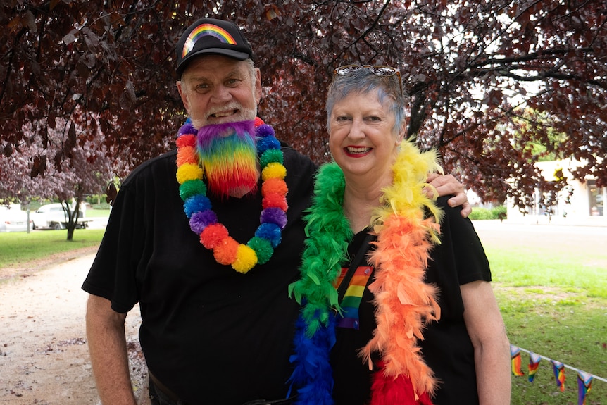 A couple adorned in rainbow coloured decorations pose together 