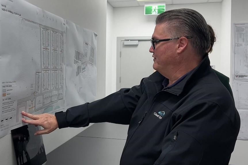 Greg with glasses in shirt that says "cloud carrier" points to a map on a wall.