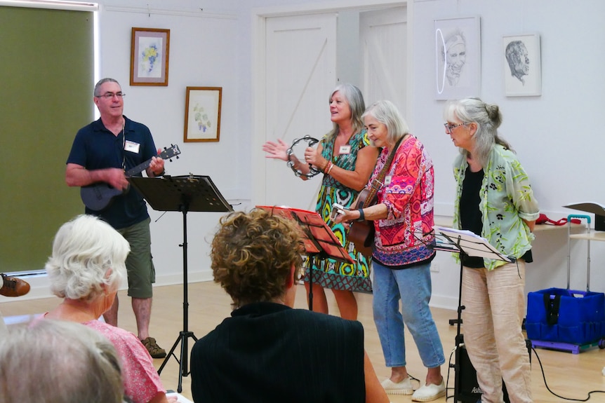 A man and three women playing guitars and tambourines in a community space.