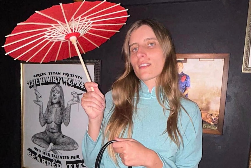 A blonde woman in a blue neck high dress holding a Parasol.