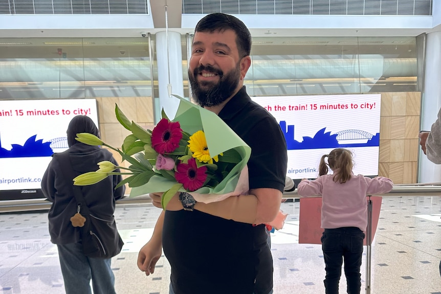 Ghanim holds a big bunch of flowers and has a wide grin at the Sydney Airport.