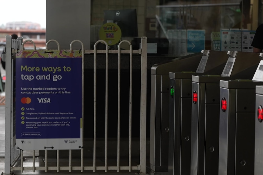 A blue poster saying "More ways to tap and go" and other information is tied to a fence beside silver machines with red Xs.