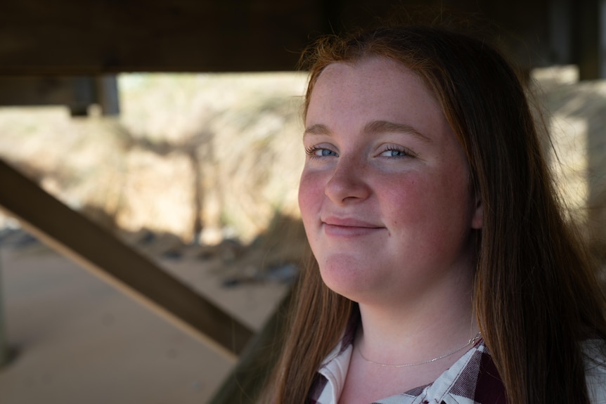 teenage girl with long brown hair and blue eyes smiles at camera