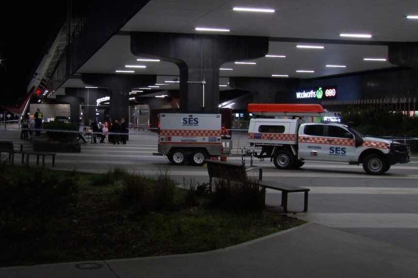 A group of police officers sit at table under a large awning near a car that says SES and a shop that says Woolworths.