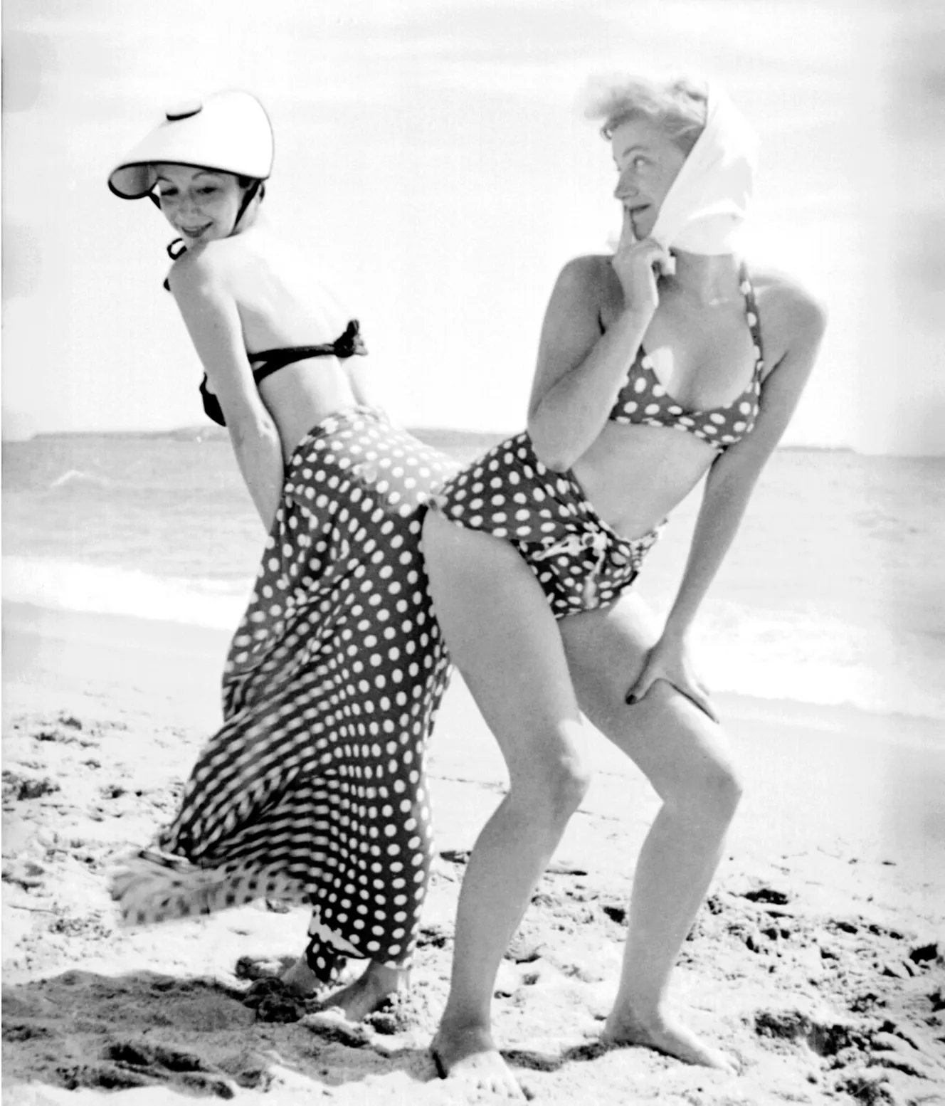 Lee Miller and an unknown woman posing in polka dot bikinis on a beach.