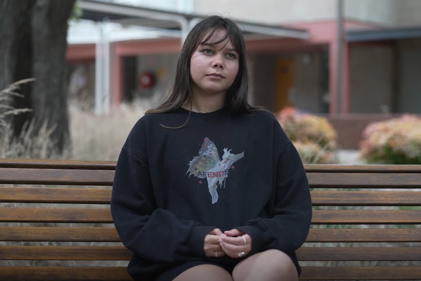 A teenage girl sits on a park bench.