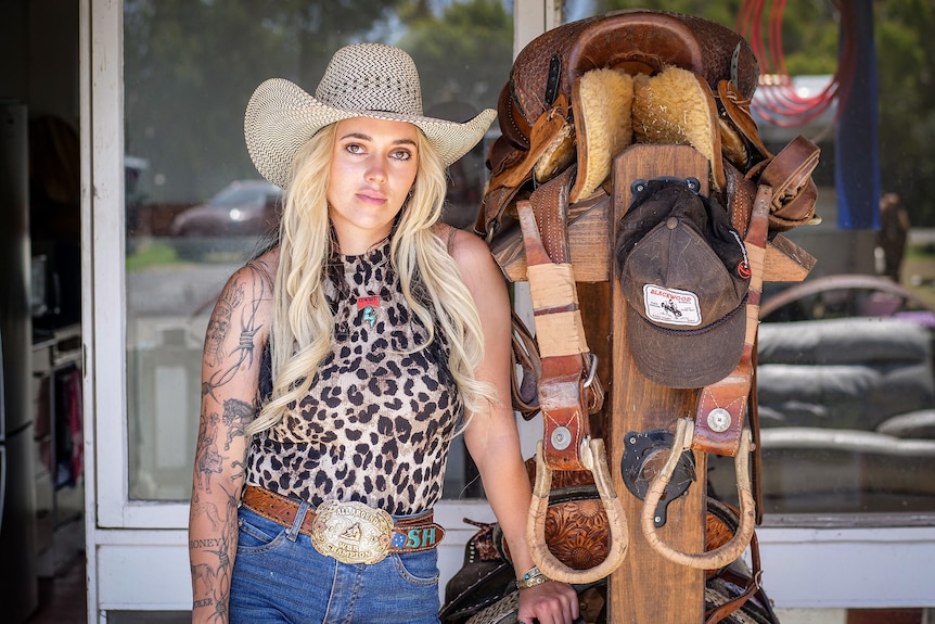 A woman standing near saddles. 