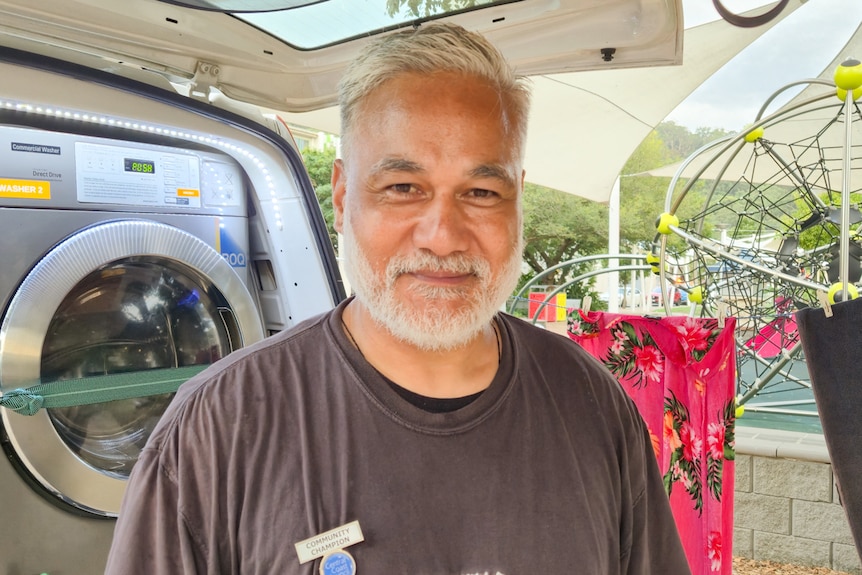 A smiling man with grey hair and beard, wears a black t-shirt.