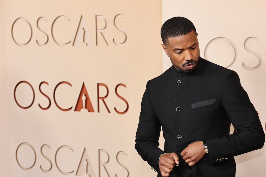 A black man in an unadorned black jacket buttoned up.