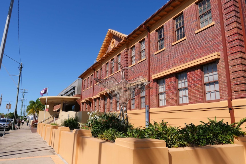 an old brick building on a sunny day with a bird statue out the front and a Queensland flag flying