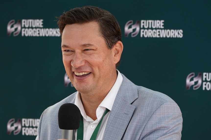 man in grey suit smiling in front of a microphone
