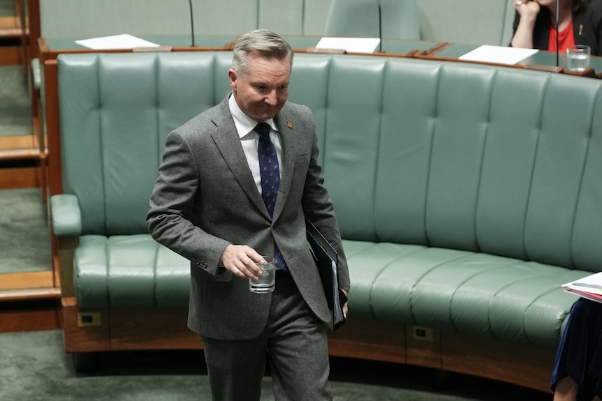 A man in a grey suit standing in parliament holding a glass of water