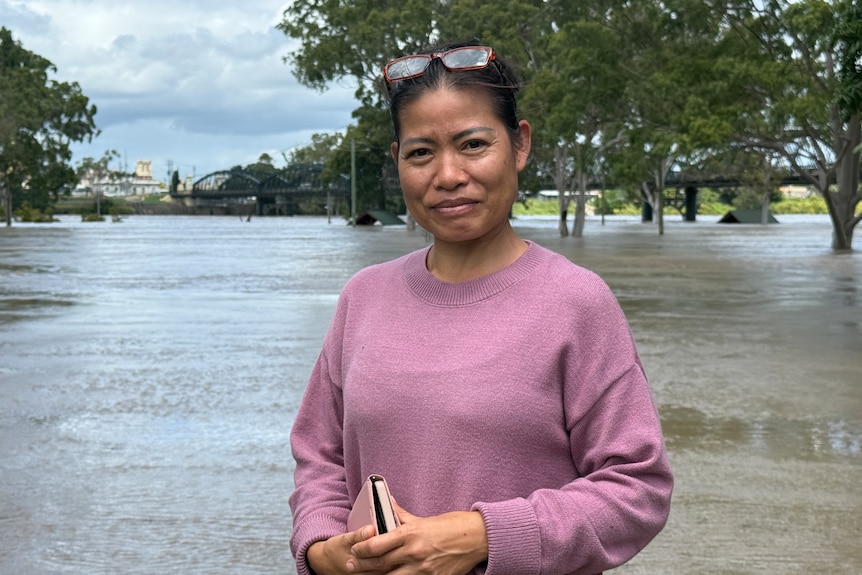 A dark-haired woman stands in front of a swollen river.