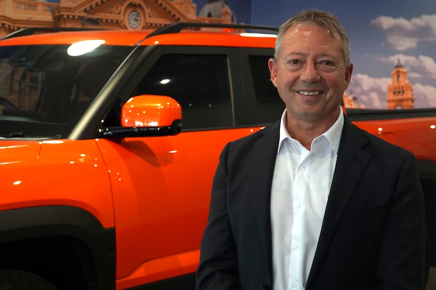 A man in suit standing beside a car in a dealership showroom.