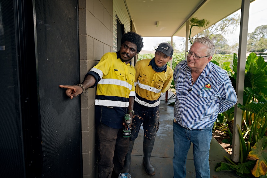 Three men look at the wall of a house.