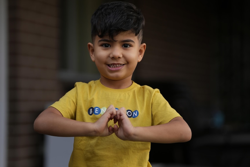 A headshot of a 4yo bo with a yellow shirt and a big smile.