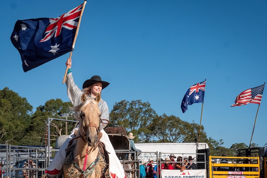 A woman riding a horse holding the Australian flag high. 