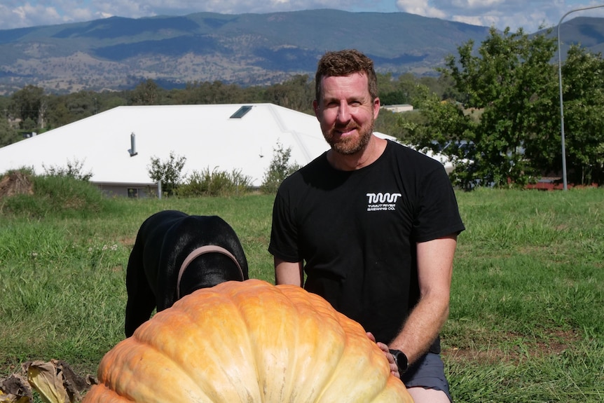 man in a black t shirt, with a pumpkin in the foreground