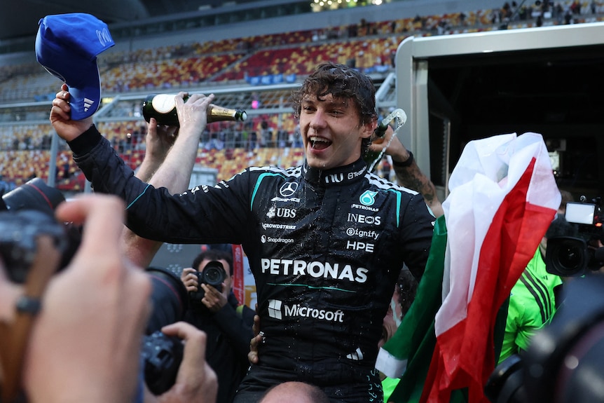 Mercedes driver Kimi Antonelli celebrates after winning the Chinese Grand Prix, holding an Italian flag, carried