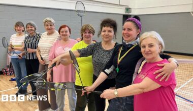 Group of women - all holding badminton rackets in their hands- smiling for the camera.