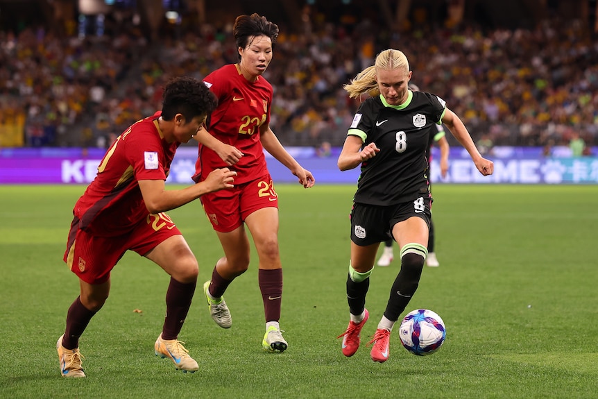 A soccer player in green runs with the ball, players in red next to her