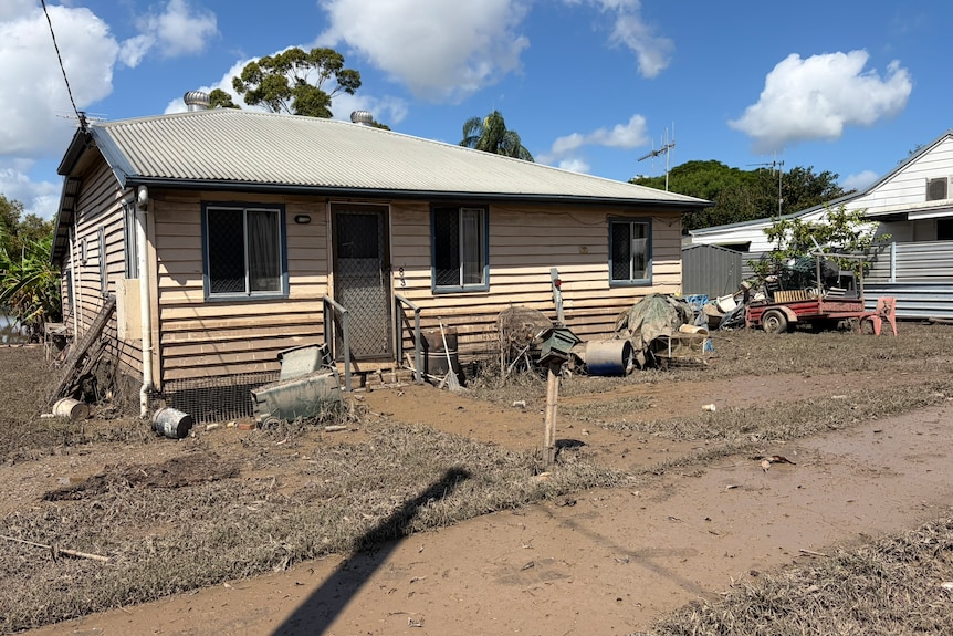 A low set weatherboard house covered in mud, with mud covering the yard and footpath