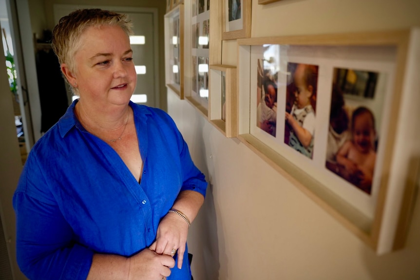 A woman with short hair and a bright blue shirt looks at framed photographs.