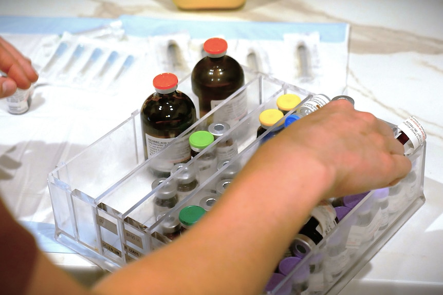 A person's arm reaches into a plastic box filled with brown bottles.