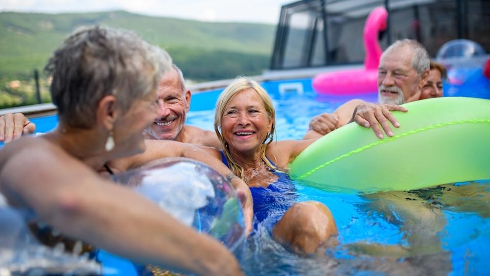 Group of cheerful seniors shaving fun in pool jumping, swiming and lounging on floats