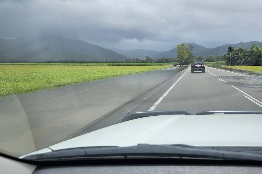 A car bonnet on a long stretch of road with storm clouds ahead. 