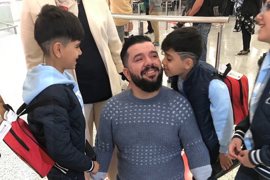 Ghanim kneels with his children and wife hugging him.