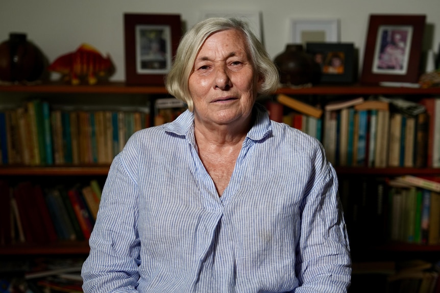 An older woman in a striped shirt sitting in front of a book shelf