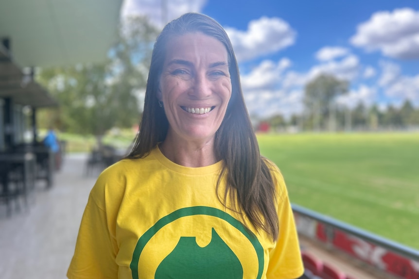 Woman in a yellow shirt standing outside a building, smiling
