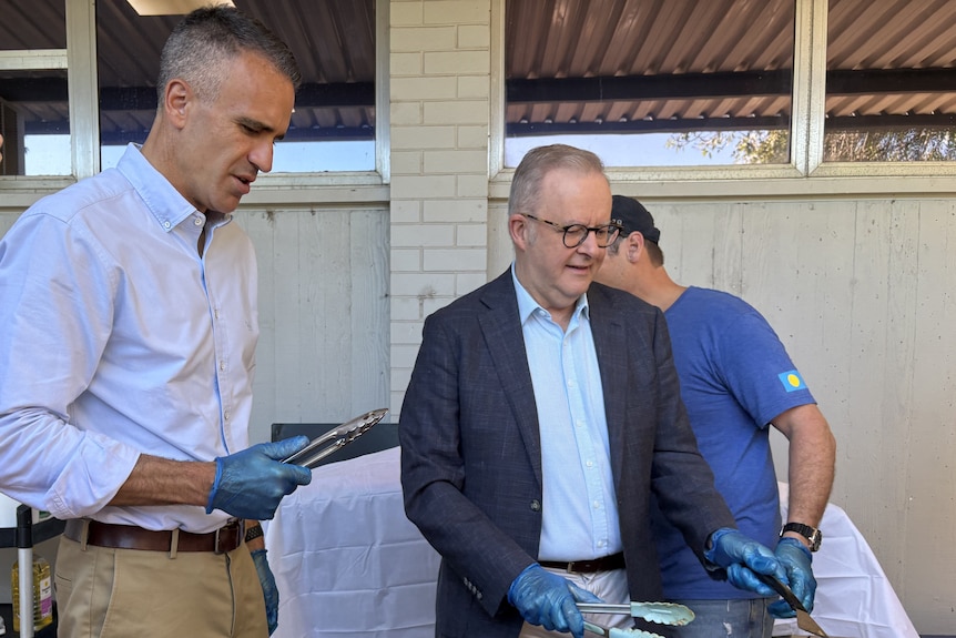 Two men cooking sausages on a barbecue