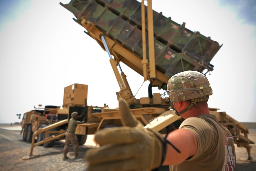 A US soldier gestures as another operates heavy machinery.
